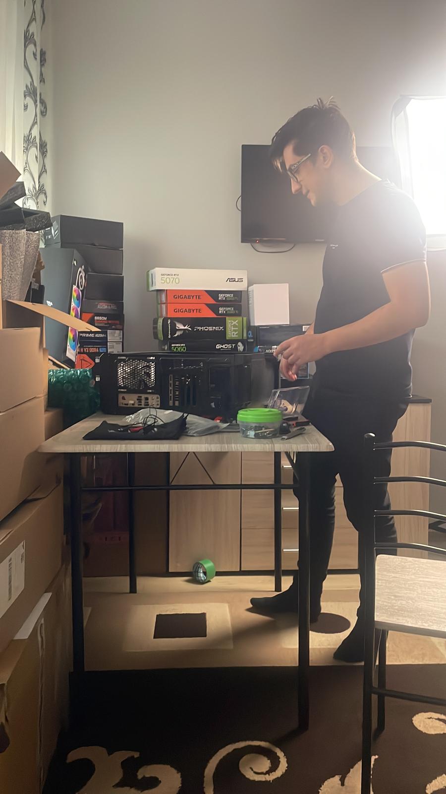 Sebastian asamblând un PC, cu cutii de plăci video pe birou